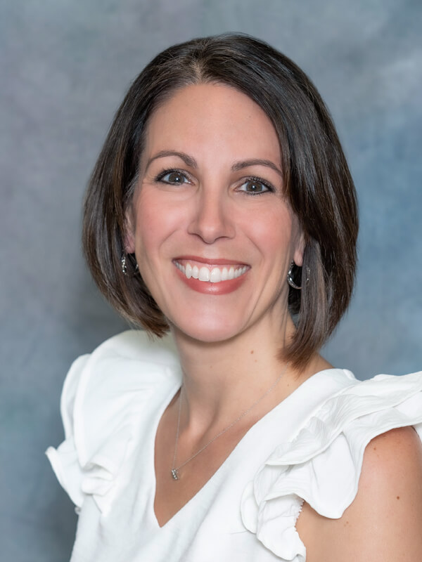 Headshot of Andrea Gravley, nurse practitioner at South Lake Pediatrics. Andrea has short brown hair, is wearing a white top with ruffled sleeves, and is smiling at the camera.