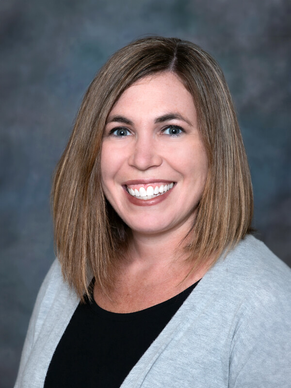 Headshot of Kathryn Douglass, nurse practitioner at South Lake Pediatrics. Kathryn has shoulder-length brown hair, is wearing a grey cardigan over a black top, and is smiling at the camera.