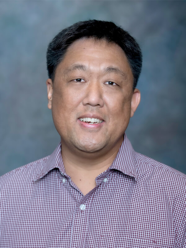 Headshot of Jason Young, pediatrician at South Lake Pediatrics. Jason has short dark hair, is wearing a checkered shirt, and is smiling at the camera.