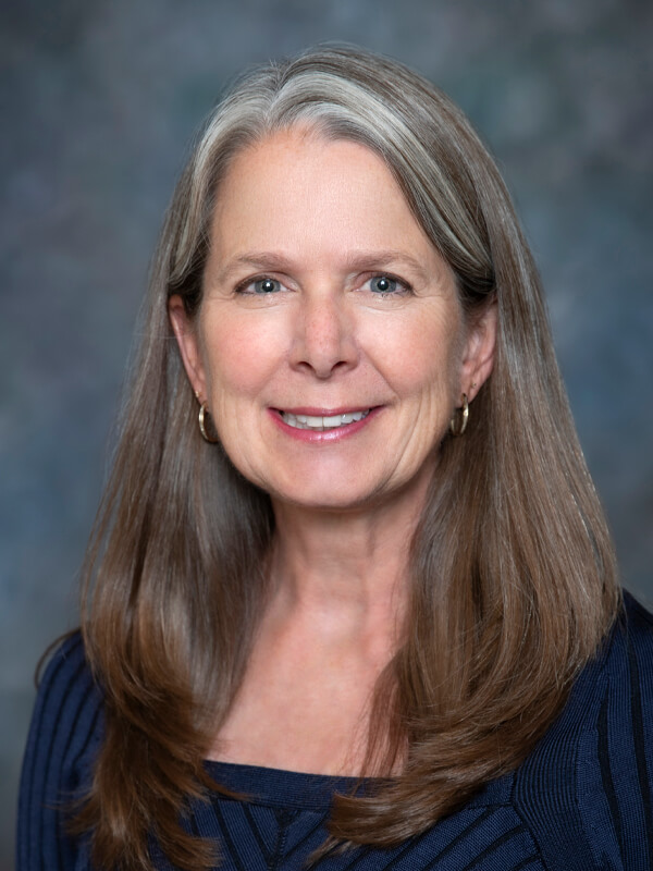 Headshot of Joanne Hoffman, pediatrician at South Lake Pediatrics. Joanne has long grey hair, is wearing a navy blue top, and is smiling at the camera.