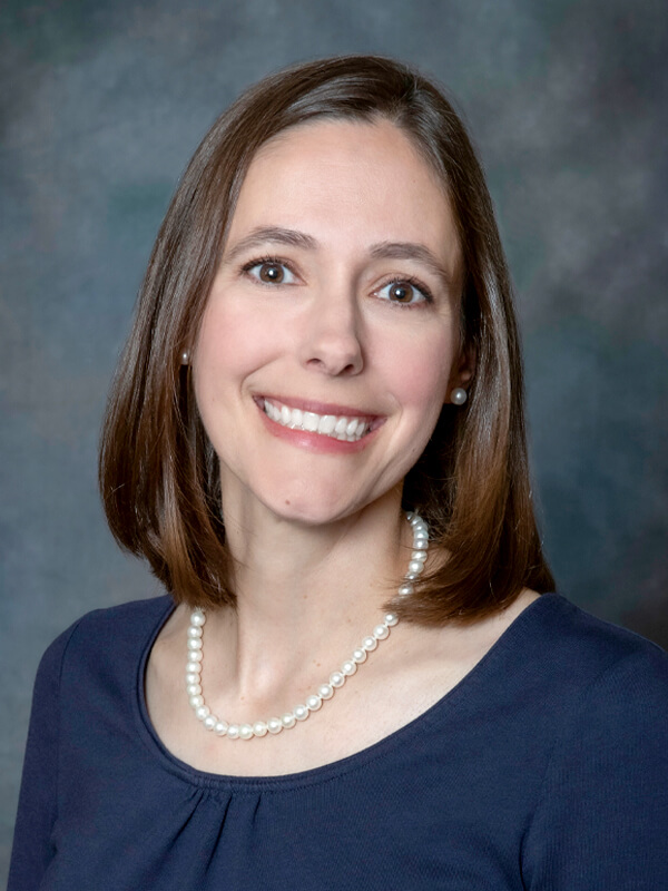 Headshot of Kristin Jakubowski, pediatrician at South Lake Pediatrics. Kristin has shoulder-length brown hair, is wearing a pearl necklace and a dark blue top, and is smiling at the camera.