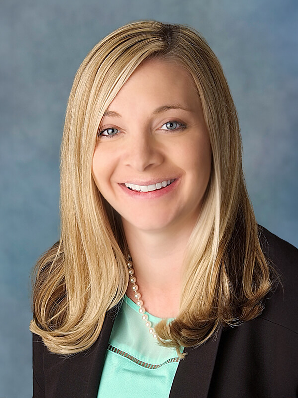 Headshot of Kyrsten Johnson, pediatrician at South Lake Pediatrics. Kyrsten has long dark hair, is wearing glasses and a blue jacket, and is smiling at the camera.