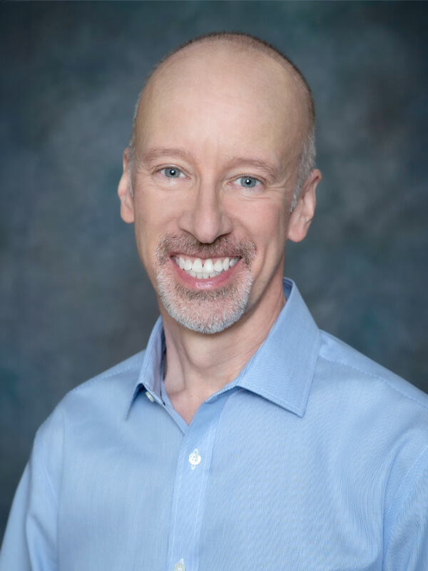 Headshot of Larry Manney, pediatrician at South Lake Pediatrics. Larry has short grey hair, is wearing a light grey polo shirt, and is smiling at the camera.