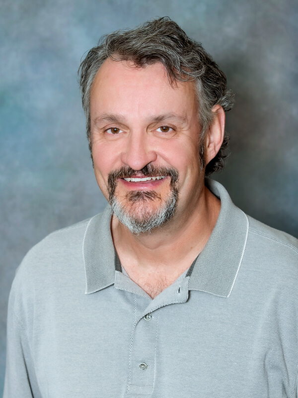 Headshot of Michael Garvis, pediatrician at South Lake Pediatrics. Michael has short brown hair, is wearing a white and blue checkered shirt, and is smiling at the camera.